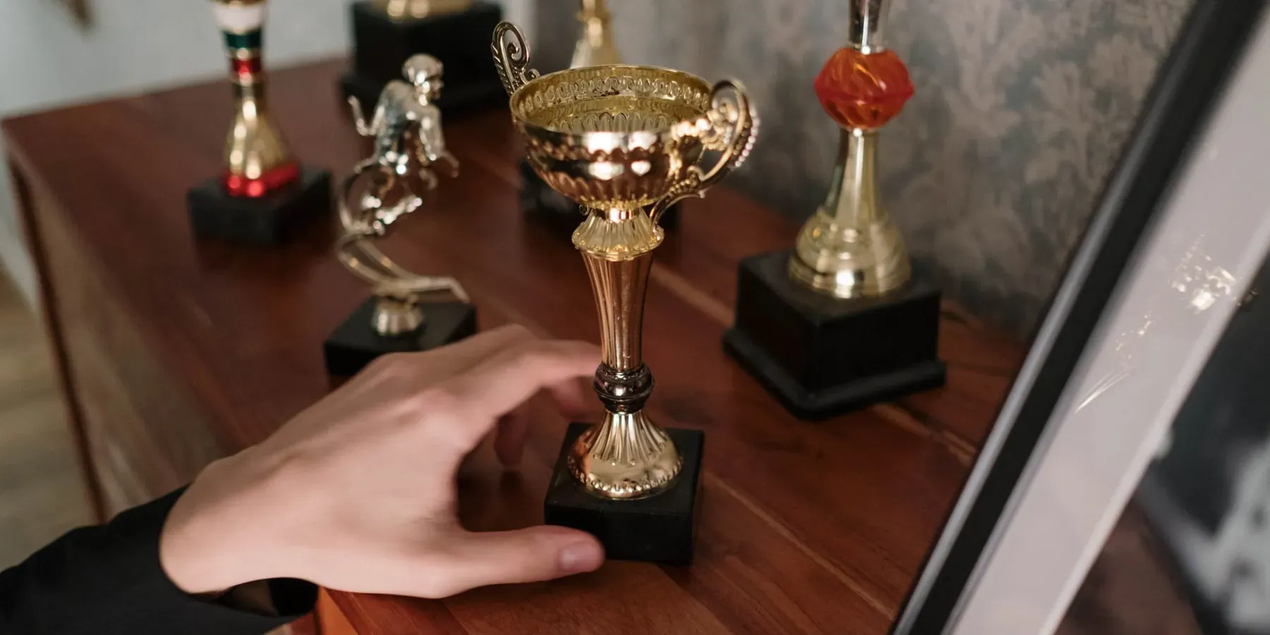 A hand reaching for an engraved trophy on a shelf of awards