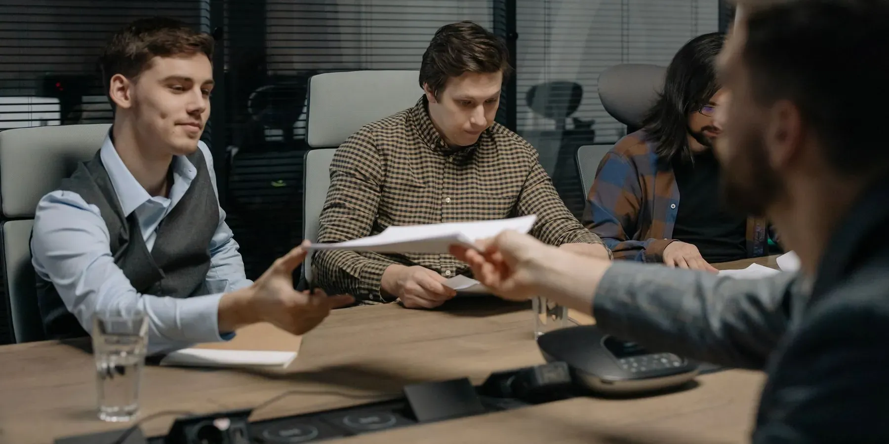 Three colleagues passing documents across a table during a project meeting
