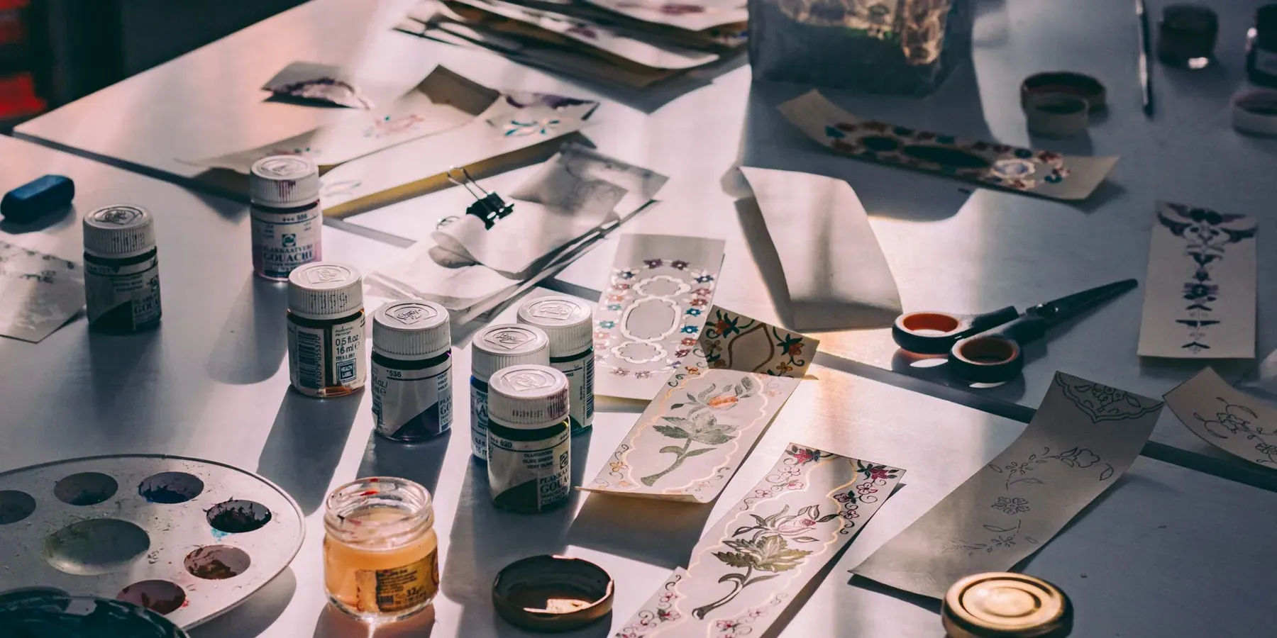 A creative workspace with paints, brushes and cut paper for a handmade project