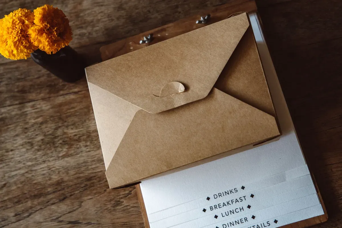 A kraft envelope and clipboard with marigold flowers on a wooden desk