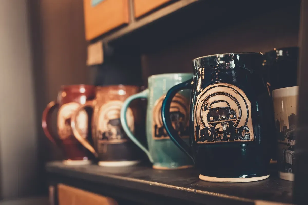 A collection of artistic ceramic mugs on a wooden shelf
