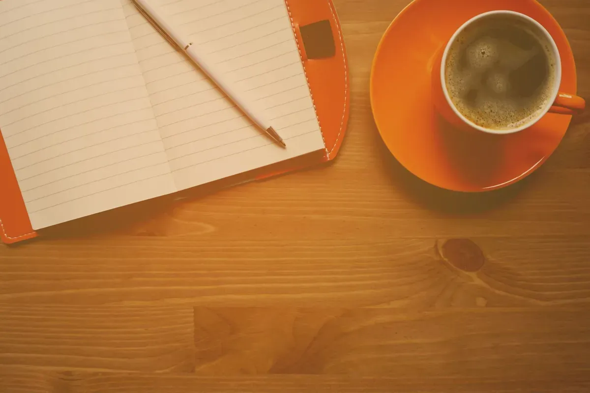 An open notebook with a fountain pen beside a cup of coffee
