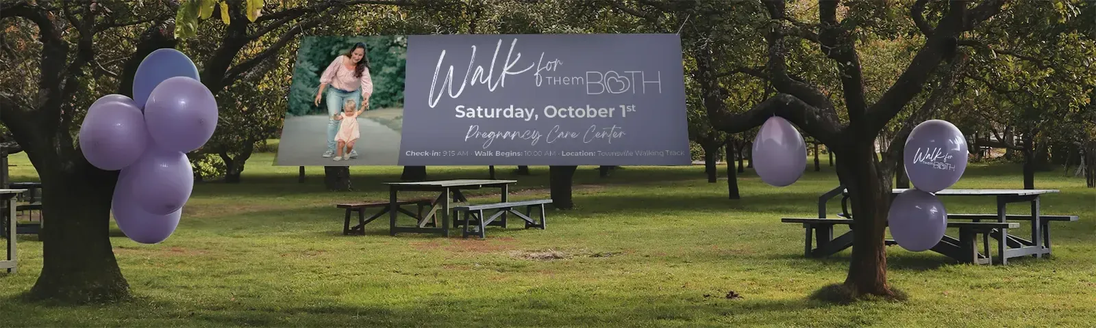 A custom outdoor event banner installed in a park, with balloons at the entrance