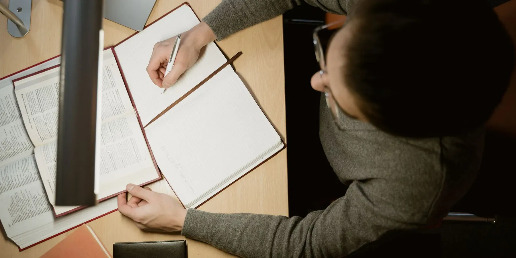 A person taking notes from open reference books at a desk
