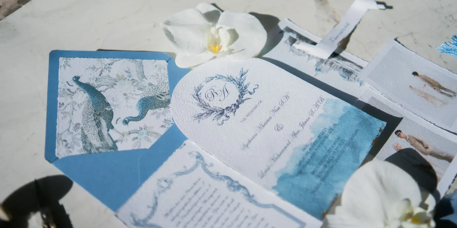 A wedding invitation suite with envelopes and an orchid on a marble surface